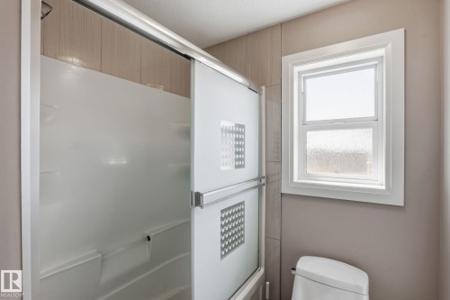 Shower enclosure with sliding frosted glass doors, a white acrylic shower surround, and light-toned tile accents - 731 57 Street Sw, Edmonton, AB - Indoor Photo Showing Bathroom