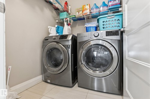 Front-loading washer and dryer set with a wire shelving system and light-toned tile flooring - 731 57 Street Sw, Edmonton, AB - Indoor Photo Showing Laundry Room