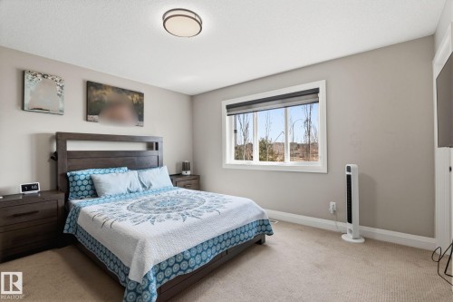 Carpeted bedroom featuring neutral wall paint, a large window with roller shades, and a flush-mount ceiling light fixture - 731 57 Street Sw, Edmonton, AB - Indoor Photo Showing Bedroom