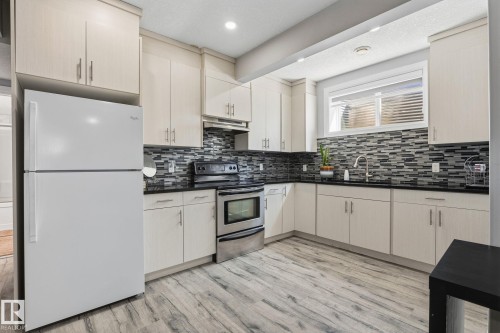 Kitchen featuring light wood-finish cabinetry, dark countertops, and a mosaic tile backsplash - 731 57 Street Sw, Edmonton, AB - Indoor Photo Showing Kitchen With Upgraded Kitchen