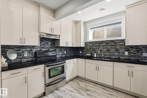 Kitchen featuring light-toned cabinetry, dark countertops, and a full tile backsplash - 731 57 Street Sw, Edmonton, AB - Indoor Photo Showing Kitchen With Upgraded Kitchen