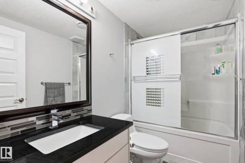Bathroom featuring a dark framed mirror, vanity with an integrated sink, dark countertop, and a mosaic tile backsplash - 731 57 Street Sw, Edmonton, AB - Indoor Photo Showing Bathroom