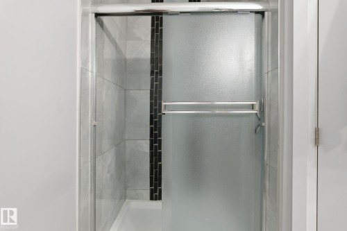 Shower enclosure with frosted glass sliding door, chrome hardware, light gray tile surround, and a vertical black mosaic tile accent strip - 731 57 Street Sw, Edmonton, AB - Indoor Photo Showing Bathroom