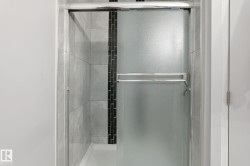 Shower enclosure with frosted glass sliding door, chrome hardware, light gray tile surround, and a vertical black mosaic tile accent strip - 