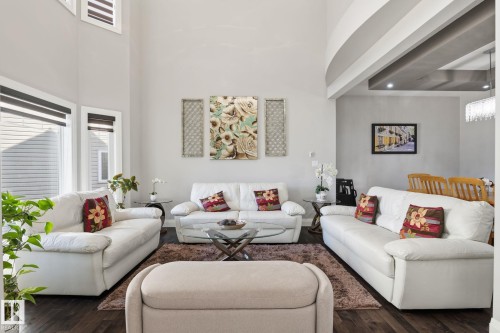 Living area featuring high ceilings, dark wood-finish flooring, multiple windows with blinds, a recessed ceiling detail, and a contemporary chandelier - 731 57 Street Sw, Edmonton, AB - Indoor Photo Showing Living Room
