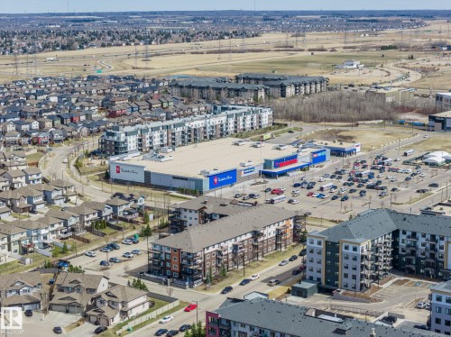 Aerial perspective showcasing a mixed-use development featuring commercial retail spaces, multi-story residential buildings, and a suburban street grid with detached housing - 731 57 Street Sw, Edmonton, AB - Outdoor With View
