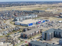 Aerial perspective showcasing a mixed-use development featuring commercial retail spaces, multi-story residential buildings, and a suburban street grid with detached housing - 