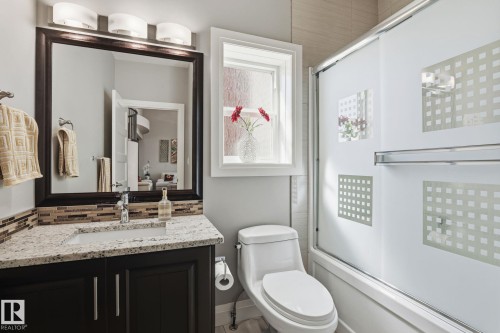 Bathroom featuring a dark wood vanity with a light-colored speckled countertop, an undermount sink, and a tiled backsplash - 731 57 Street Sw, Edmonton, AB - Indoor Photo Showing Bathroom