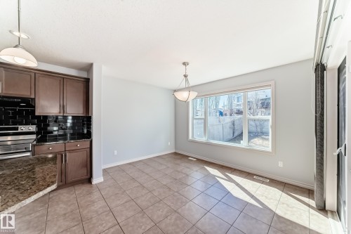 Bright dining area featuring a large window, tiled flooring, and a contemporary chandelier - 6723 19 Avenue, Edmonton, AB 