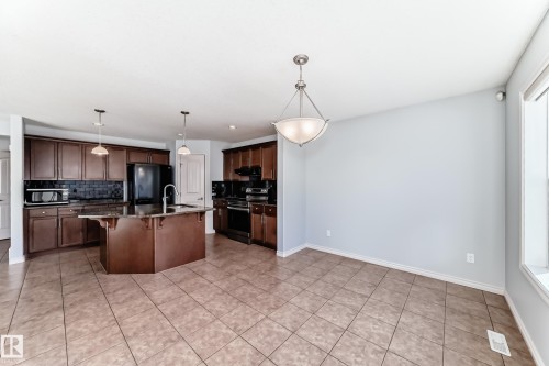 Spacious kitchen and dining area featuring a central island, dark wood-finish cabinetry, tile flooring, and a large window - 6723 19 Avenue, Edmonton, AB 