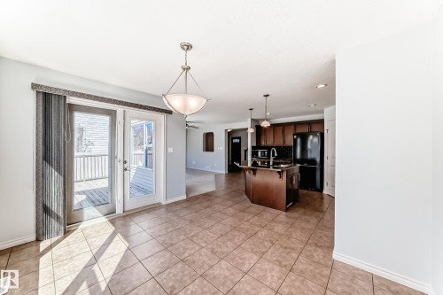 Dining area with ceramic tile flooring, double French doors leading to a deck, and an adjacent kitchen featuring a central island with a sink, dark cabinetry, and black appliances - 6723 19 Avenue, Edmonton, AB 
