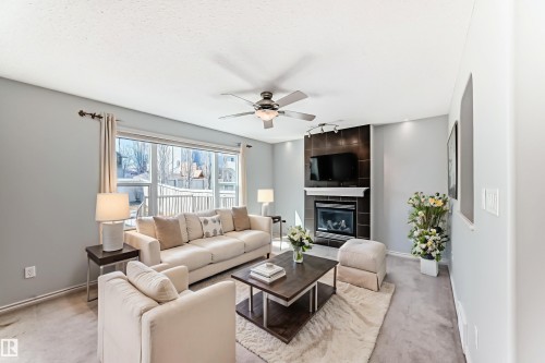 Living area with a corner fireplace, large window, ceiling fan, and light gray wall paint - 6723 19 Avenue, Edmonton, AB 