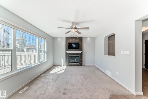 Living area featuring a gas fireplace with a tiled surround and white mantel, a ceiling fan with integrated lighting, and a large picture window - 6723 19 Avenue, Edmonton, AB 