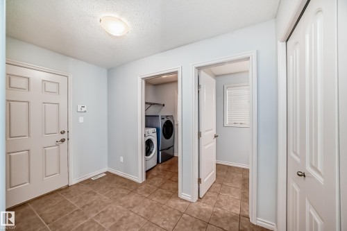Functional utility area featuring a front-loading washer and dryer, tiled flooring, light blue wall paint, white trim, and a white paneled door - 6723 19 Avenue, Edmonton, AB 