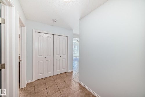 Hallway featuring neutral wall paint, tiled flooring, white bi-fold closet doors, and white baseboards - 6723 19 Avenue, Edmonton, AB 