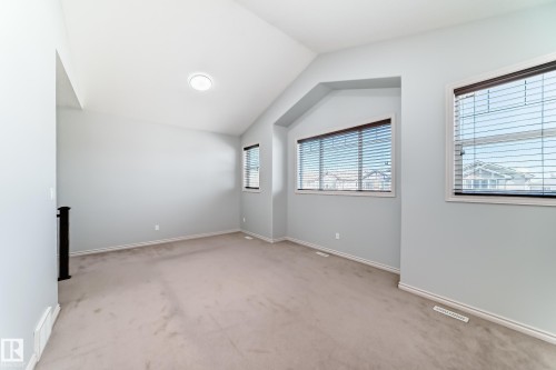 Spacious room featuring vaulted ceilings, light-colored carpeting, multiple windows with blinds, a black newel post, and baseboard trim - 6723 19 Avenue, Edmonton, AB 