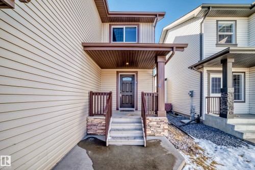 Covered entryway featuring a dark wood-finish door, stone-accented pillars, and matching wood-finish railings - 6723 19 Avenue, Edmonton, AB 