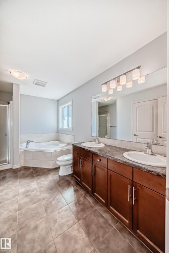 Bathroom featuring a dual vanity with wood-finish cabinetry, a large built-in mirror, a corner jetted tub, and a separate shower enclosure - 6723 19 Avenue, Edmonton, AB 