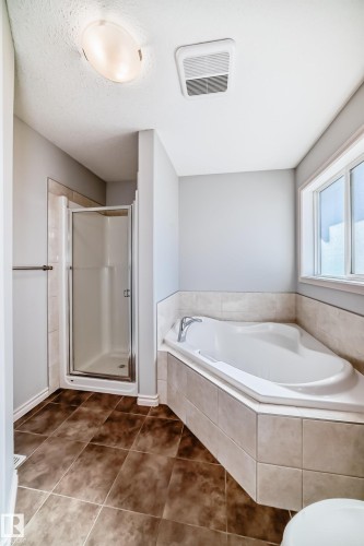 Corner soaking tub with tiled surround, walk-in shower with glass enclosure, brown tile flooring, and a large window - 6723 19 Avenue, Edmonton, AB 