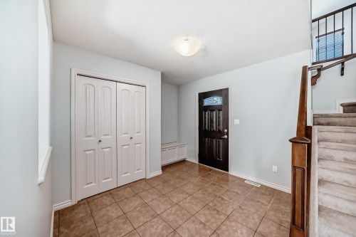 Entryway featuring tile flooring, a dark wood front door with decorative glass, white bi-fold closet doors, a built-in bench, and a carpeted staircase with a wood railing - 6723 19 Avenue, Edmonton, AB 