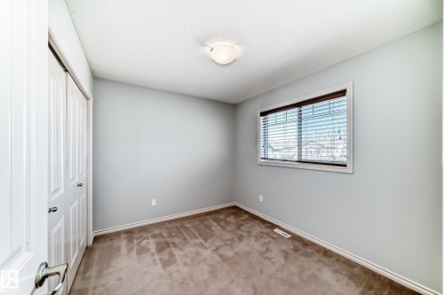 Carpeted room featuring a window with blinds, bi-fold closet doors, and light gray walls - 6723 19 Avenue, Edmonton, AB 