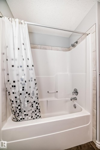 Bathtub and shower combination featuring a white composite surround, chrome fixtures, and a tile accent border - 6723 19 Avenue, Edmonton, AB 