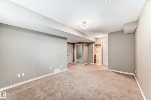 Spacious room featuring neutral carpeting, light gray walls, white baseboards, and a semi-flush mount ceiling light - 6723 19 Avenue, Edmonton, AB 