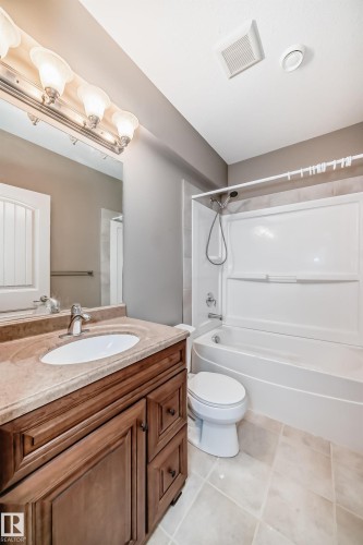 Bathroom featuring a wood-finish vanity with a built-in sink, a light-toned countertop, and a vanity light fixture - 6723 19 Avenue, Edmonton, AB 