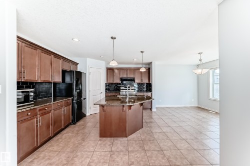 Kitchen featuring an angled island with a double basin sink, stone-finish countertops, dark subway tile backsplash, and coordinating wood-finish cabinetry - 6723 19 Avenue, Edmonton, AB 