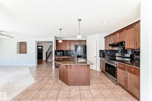 Spacious kitchen featuring an island with a built-in sink, granite countertops, wood cabinetry, and stainless steel appliances - 6723 19 Avenue, Edmonton, AB 