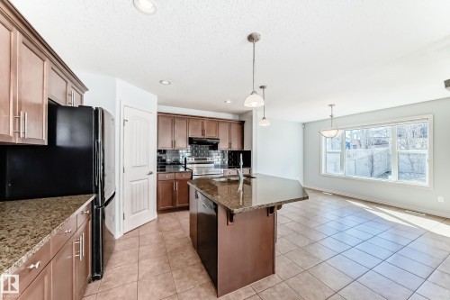 Open-concept kitchen featuring an island with a sink, pendant lighting, warm wood cabinetry, granite countertops, and tile flooring - 6723 19 Avenue, Edmonton, AB 