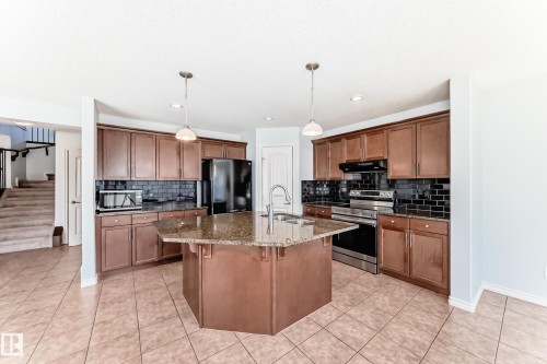 Kitchen featuring a hexagonal island with granite countertop and undermount sink, pendant lighting, stainless steel appliances, and dark subway tile backsplash - 6723 19 Avenue, Edmonton, AB 