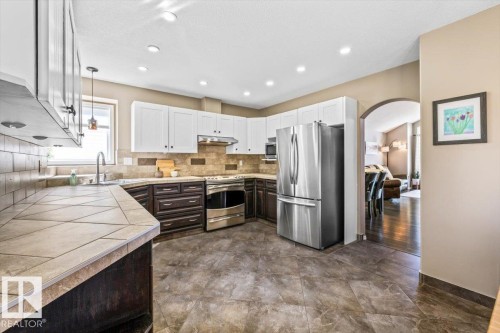 Kitchen featuring a combination of white upper cabinetry and dark wood-finish lower cabinetry, stainless steel appliances, a tile backsplash, and a large window above the sink - 86 Westpark Way, Fort Saskatchewan, AB - Indoor Photo Showing Kitchen With Stainless Steel Kitchen