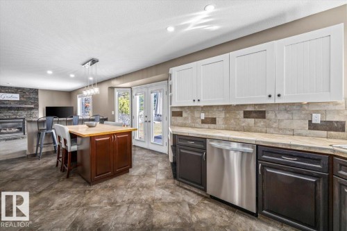 Kitchen featuring two-tone cabinetry, stainless steel dishwasher, tile flooring, and a stone-clad fireplace - 86 Westpark Way, Fort Saskatchewan, AB - Indoor Photo Showing Kitchen