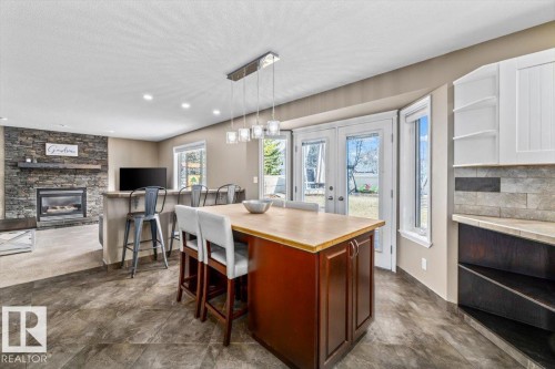 Spacious kitchen and living area featuring tile flooring, a central island with seating, pendant lighting, and a stone-clad fireplace - 86 Westpark Way, Fort Saskatchewan, AB - Indoor Photo Showing Dining Room With Fireplace
