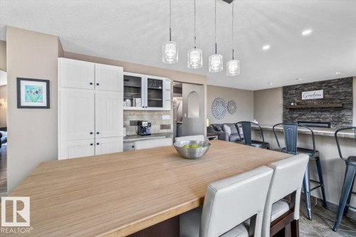 Kitchen island with a light wood-finish countertop, pendant lighting, white cabinetry, and a stone backsplash - 86 Westpark Way, Fort Saskatchewan, AB - Indoor