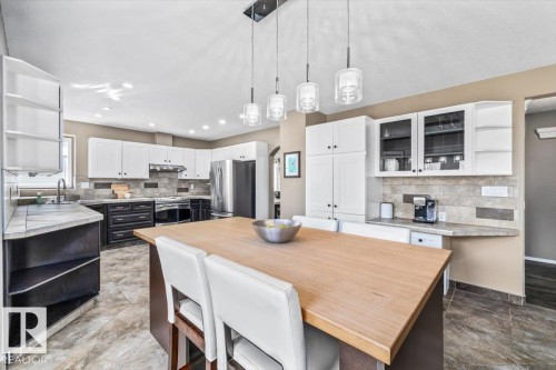 Spacious kitchen featuring a large central island with a wood-finish countertop, pendant lighting, and tiled flooring - 86 Westpark Way, Fort Saskatchewan, AB - Indoor Photo Showing Kitchen With Upgraded Kitchen