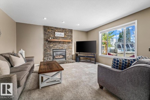 Living area featuring a stone-clad fireplace with a wood mantel, a large picture window, recessed lighting, and neutral carpeting - 86 Westpark Way, Fort Saskatchewan, AB - Indoor Photo Showing Living Room With Fireplace