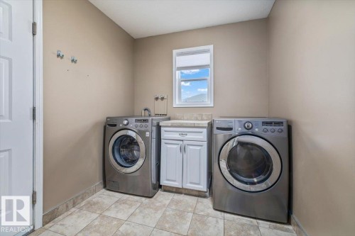 Laundry area featuring square tiled flooring, a window, a white base cabinet with a countertop, and neutral wall paint - 86 Westpark Way, Fort Saskatchewan, AB - Indoor Photo Showing Laundry Room
