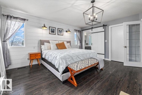 Spacious room featuring dark wood-finish flooring, white shiplap accent wall, and a rustic industrial chandelier - 86 Westpark Way, Fort Saskatchewan, AB - Indoor Photo Showing Bedroom