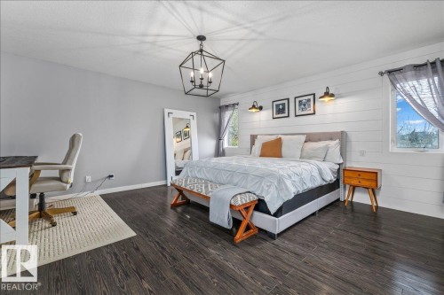 Spacious sleeping quarters featuring dark wood-finish flooring and a geometric ceiling light fixture - 86 Westpark Way, Fort Saskatchewan, AB - Indoor Photo Showing Bedroom