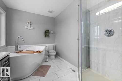 Freestanding soaking tub with chrome floor-mounted faucet, glass-enclosed shower featuring white tiled walls, and white rectangular floor tiles - 86 Westpark Way, Fort Saskatchewan, AB - Indoor Photo Showing Bathroom