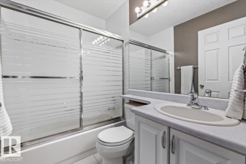 Full bathroom featuring a shower-tub combination with frosted sliding glass doors, white subway tile surround, white vanity with integrated sink, chrome faucet, and mirrored wall - 86 Westpark Way, Fort Saskatchewan, AB - Indoor Photo Showing Bathroom