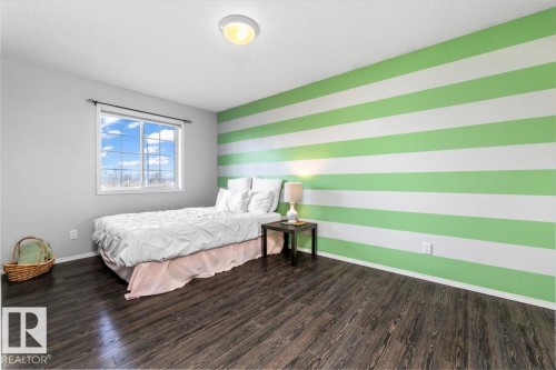 Room featuring a horizontal striped accent wall, a multi-pane window, and wood-finish flooring - 86 Westpark Way, Fort Saskatchewan, AB - Indoor Photo Showing Bedroom