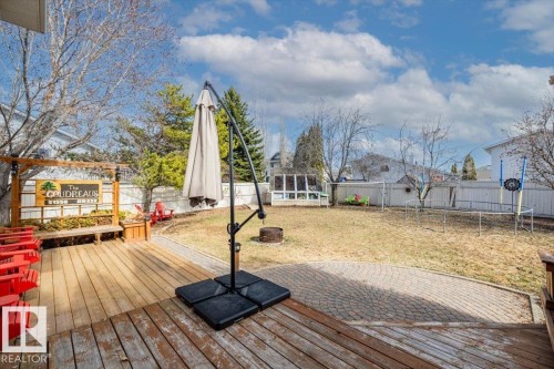Expansive backyard featuring a wood deck, circular paver patio, a wooden pergola structure, and a fenced perimeter - 86 Westpark Way, Fort Saskatchewan, AB - Outdoor With Deck Patio Veranda