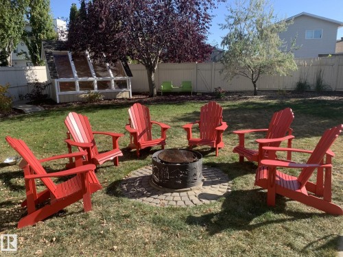 Expansive backyard featuring a central fire pit with paver surround, a greenhouse structure, mature trees, and a wood privacy fence - 86 Westpark Way, Fort Saskatchewan, AB - Outdoor