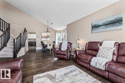 Open-concept living space featuring wood-finish flooring, vaulted ceilings, and a staircase with dark wood railings - 86 Westpark Way, Fort Saskatchewan, AB - Indoor Photo Showing Living Room