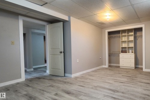 Spacious room featuring wood-finish flooring, a built-in closet system with shelving and drawers, neutral wall paint, white trim, and a drop-tile ceiling with recessed lighting - 4911 106 Street, Edmonton, AB - Indoor Photo Showing Other Room