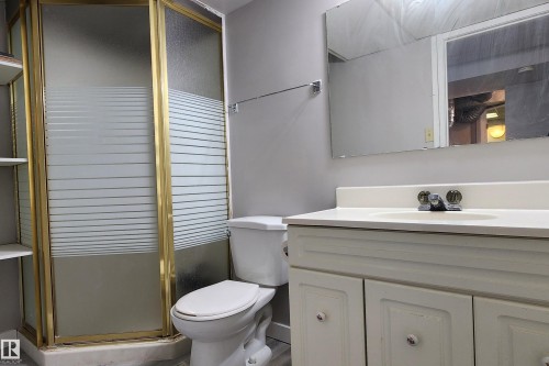Bathroom featuring a glass shower enclosure with gold-tone framing, a single vanity with storage, and an integrated sink - 4911 106 Street, Edmonton, AB - Indoor Photo Showing Bathroom