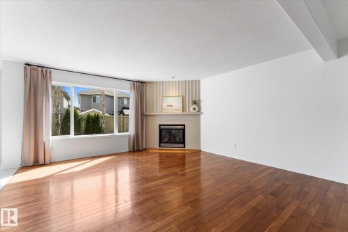 Hardwood flooring throughout a spacious room featuring a corner fireplace with a white mantel and a large picture window - 326 Silver Berry Road, Edmonton, AB - Indoor Photo Showing Living Room With Fireplace